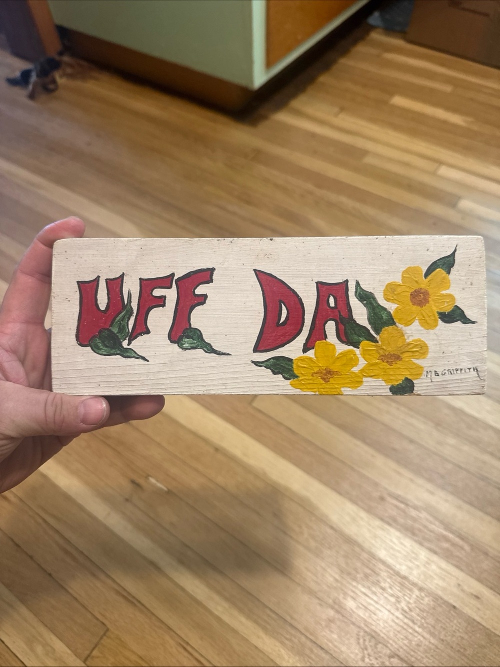 Vintage hand-painted wooden "Uff Da" sign accented with yellow wildflowers MN
